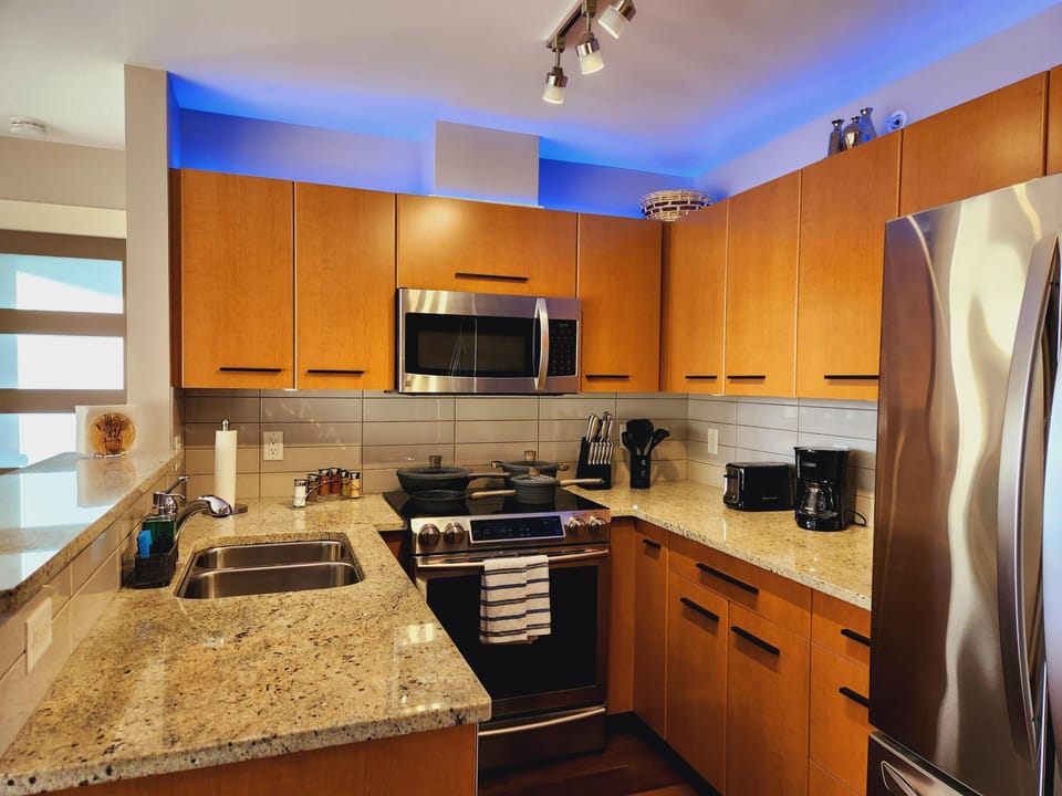 Granite countertops and light wood cabinets surround stainless steel appliances in the compact kitchen.
