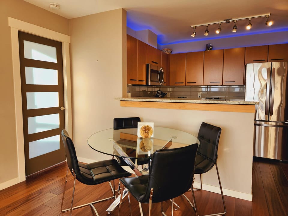 Glass-top dining table surrounded by four black leather chairs on warm wood floors.