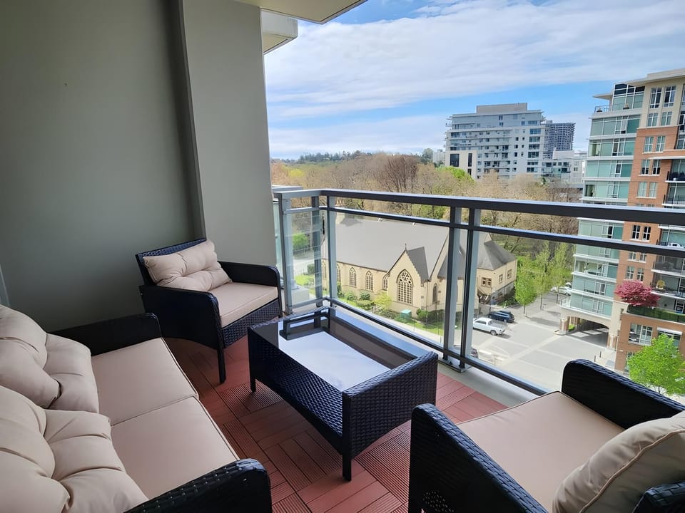 Balcony seating with black wicker furniture and beige cushions overlooks a city street and historic church.