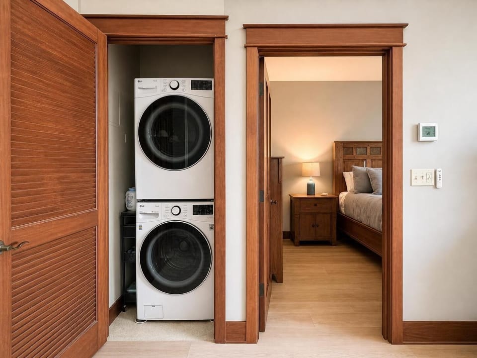In-unit stacked LG washer/dryer in louvered closet, steps from the warmly lit bedroom — pack light, stay longer