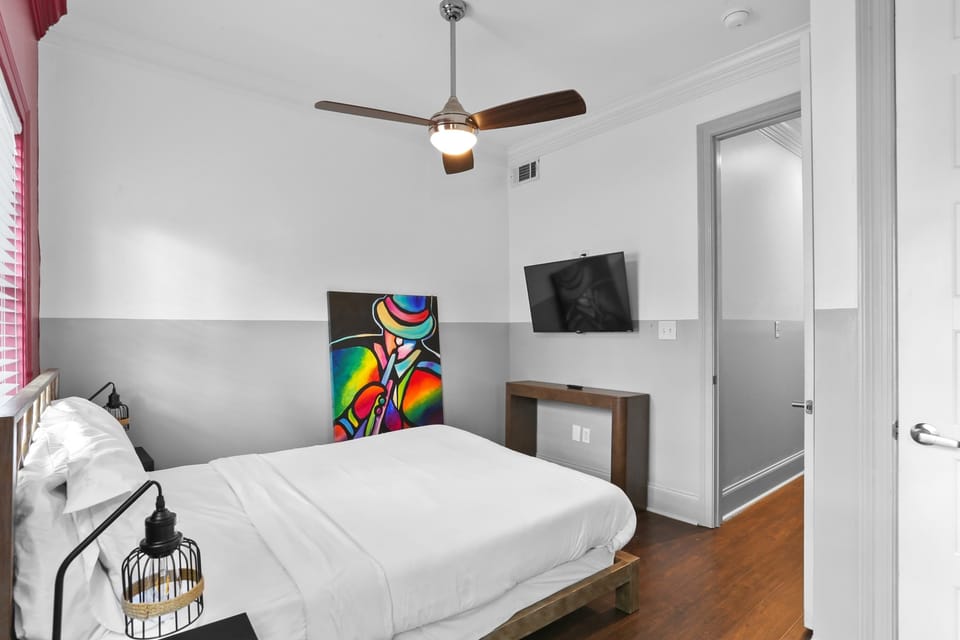 Cozy queen bedroom with a ceiling fan, Smart TV, natural light, and colorful artwork for a cheerful, comfortable retreat.