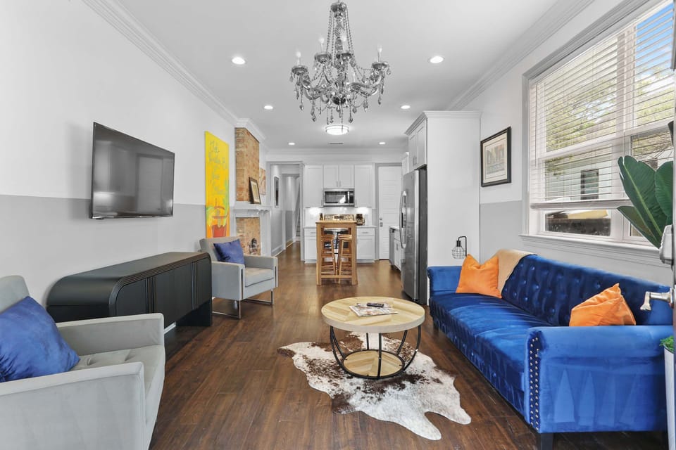 Bright, inviting living room with comfortable seating, colorful New Orleans-inspired décor, hardwood floors, and an open layout connecting to the dining and kitchen areas.