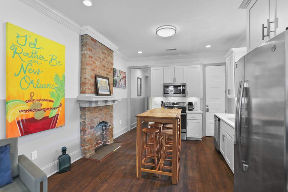 Open kitchen and dining area featuring exposed brick, colorful artwork, hardwood floors, and an island with seating for four.