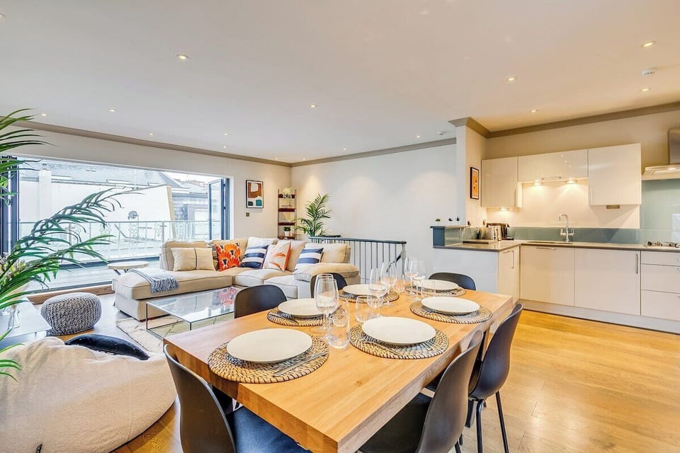 Open plan living room with kitchen and dining table. Opening onto large balcony terrace, which has outdoor seating.