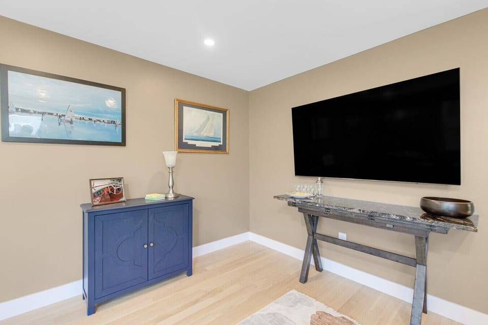 Detailed view of the TV wall setup paired with a blue two-door storage cabinet, lamps, and framed nautical wall art.