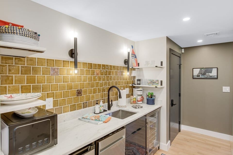 Overview of the kitchenette counter with white marble countertops, a wine fridge, dishwasher, microwave, and olive-green tile backsplash.