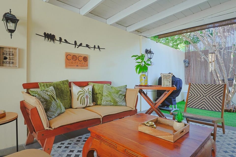 Slow down on this breezy covered patio with botanical seating, warm wood accents, lush greenery, and space to relax.