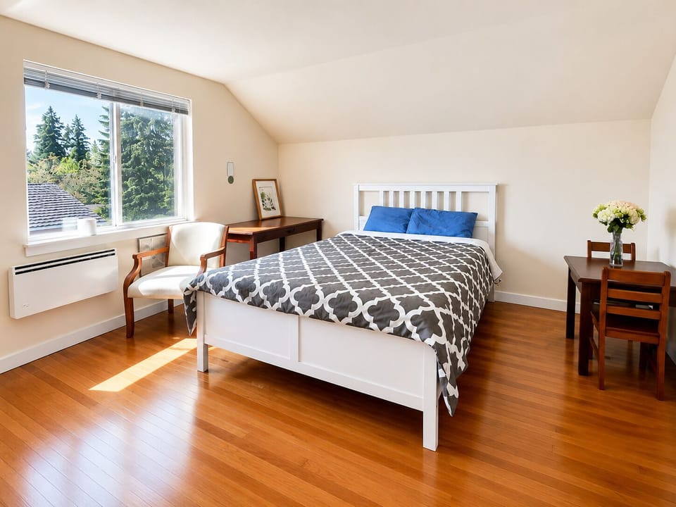 Bright, airy bedroom with hardwood floors, desk, and peaceful tree views