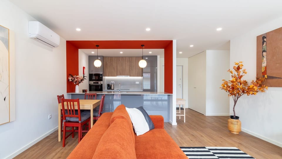 Gather around the cozy dining table for a delicious meal, or relax on the vibrant sofa in this inviting open-concept living space, thoughtfully designed for both comfort and social interaction. The bright red accents add a playful touch to your stay. #Fam
