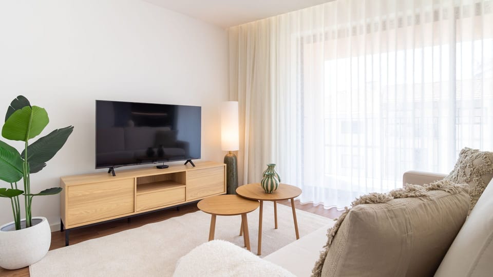 Relax in the bright and airy living area, featuring a comfortable sofa and a large TV for your entertainment, perfect for unwinding after a day of exploration. Enjoy the serene ambiance created by the sheer curtains filtering natural light, making it an i