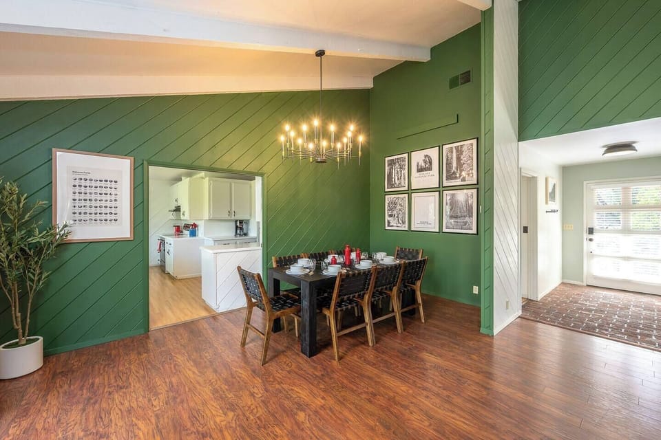 Gather around this stylish dining space featuring rich wood floors, a modern chandelier, and a bold green accent wall that opens seamlessly to the kitchen. Perfect for shared meals and conversation.