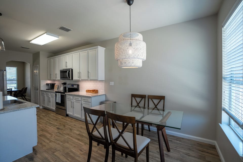 Bright dining area with glass table, designer lighting, and modern kitchen