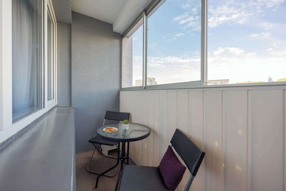 The balcony offers a quiet spot with large windows providing plenty of natural light. A small round table paired with folding chairs creates a functional setting for an outdoor coffee or rest