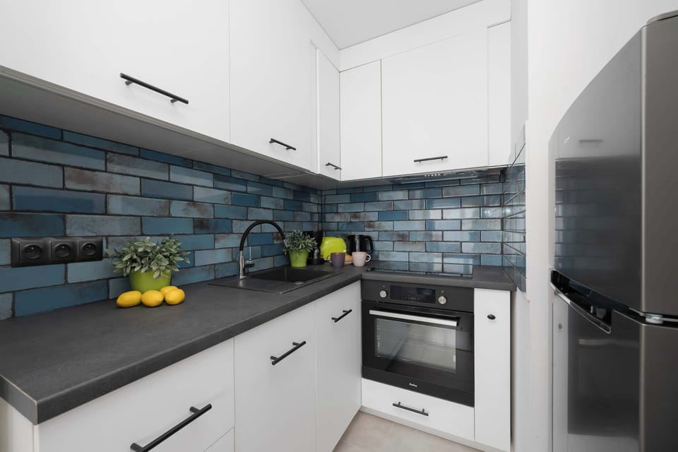 The kitchenette is designed with modern white cabinetry, dark countertops, and integrated appliances including an oven and stovetop. Blue glossy subway tiles on the backsplash bring a distinctive color accent to the space.