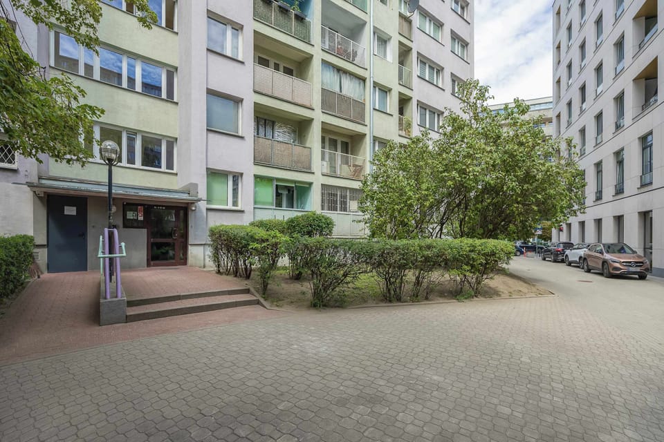 The ouside of the residential building includes paved walkways and green landscaping. Manicured bushes and mature trees offer a pleasant environment right outside the property.