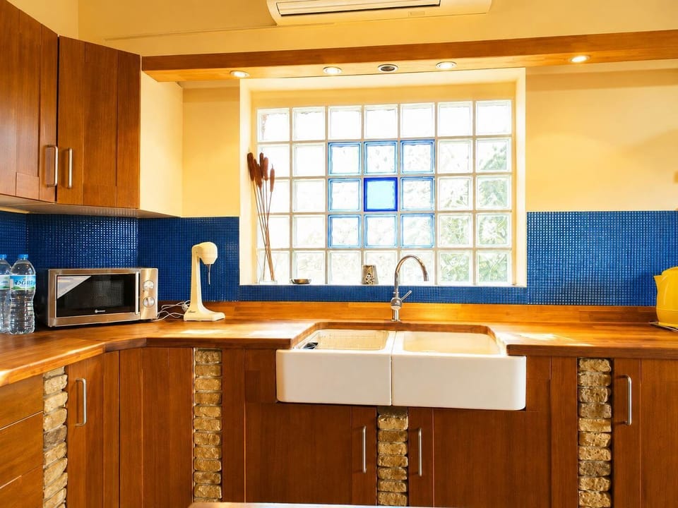 A practical kitchen with wooden cabinets, tiled work surfaces, a large sink and a bright window that fills the space with light while making breakfast, lunch or dinner
