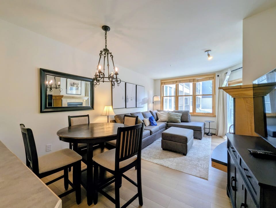 Step into your bright, open living space where natural light streams through large windows. A cozy sectional and dining nook create the perfect home base for relaxing after mountain adventures.