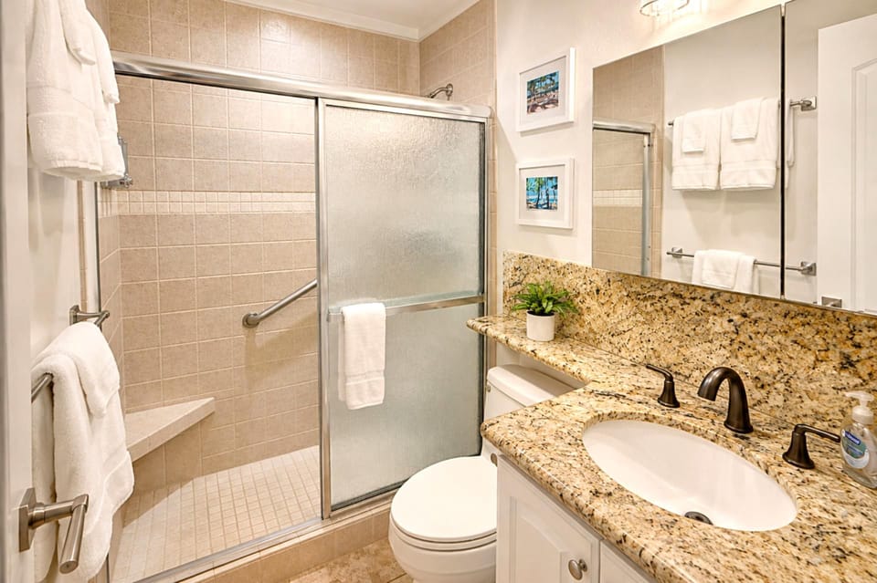 The granite-topped vanity and walk-in glass shower keep things bright and easy -- a sliding glass door, built-in shower seat and grab bar, plush white towels, and a touch of tropical wall art to set the mood.