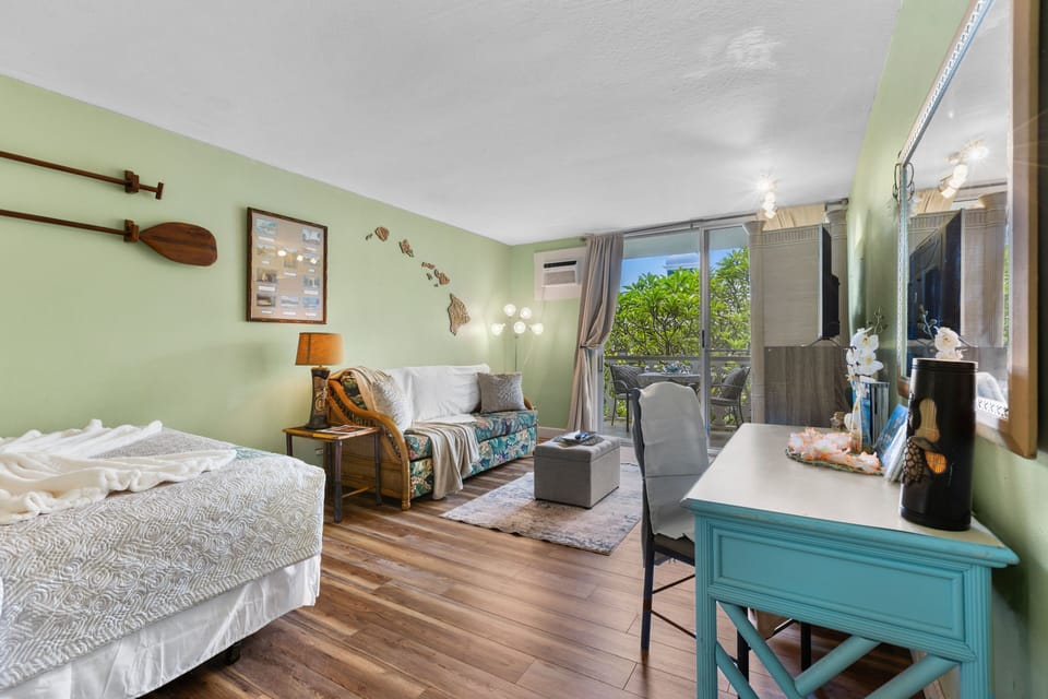 A studio living space featuring light green walls, a desk, a sofa, and balcony access.