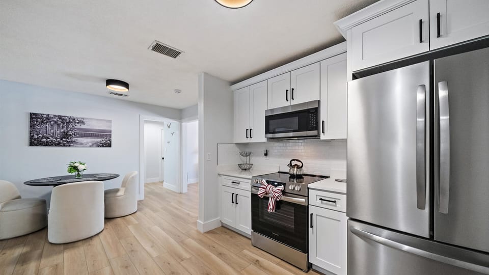 Your modern kitchen features sleek stainless appliances, bright white cabinetry, and warm wood floors that flow seamlessly into your dining space—perfect for cooking and gathering.