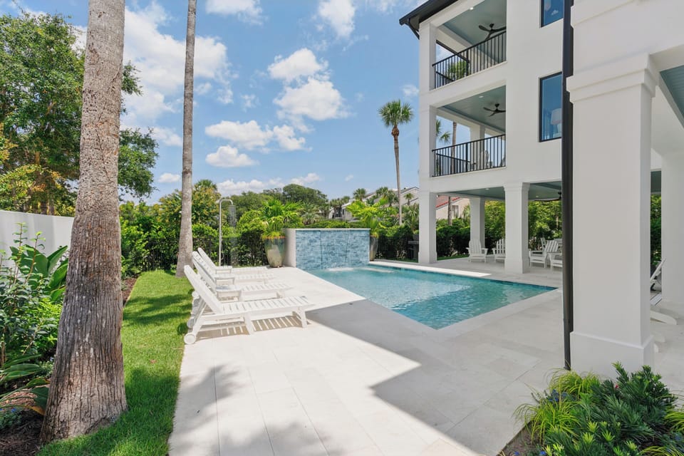 Stunning pool oasis framed by lush palms and modern waterfall feature, with spacious lounging deck inviting endless sunny afternoons.