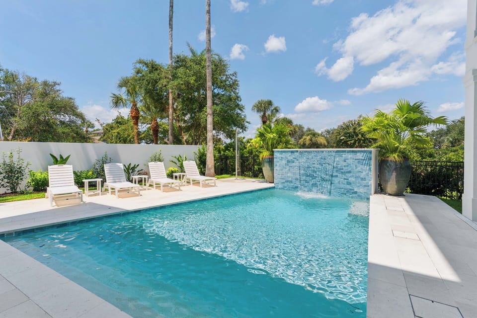 A sparkling pool with a stunning waterfall feature awaits in your private backyard oasis, surrounded by lush tropical landscaping and plenty of lounge chairs for sun-soaked relaxation.