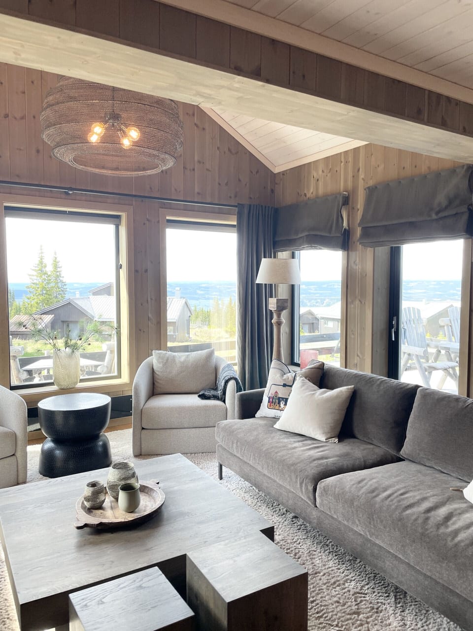 Cozy living room filled with natural light and large windows offering beautiful views of the surrounding landscape, creating a warm and inviting cabin atmosphere.