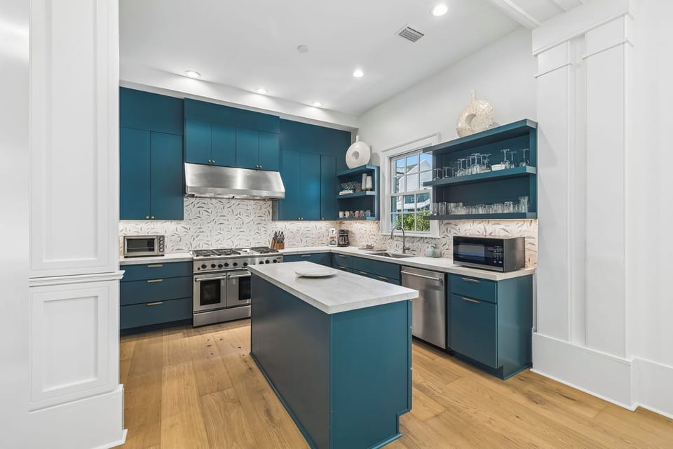 Step into a chef's dream kitchen with sleek blue cabinetry, stainless steel appliances, and a bright center island ready for your culinary creations. The elegant backsplash and open shelving add style and convenience to every meal you prepare.