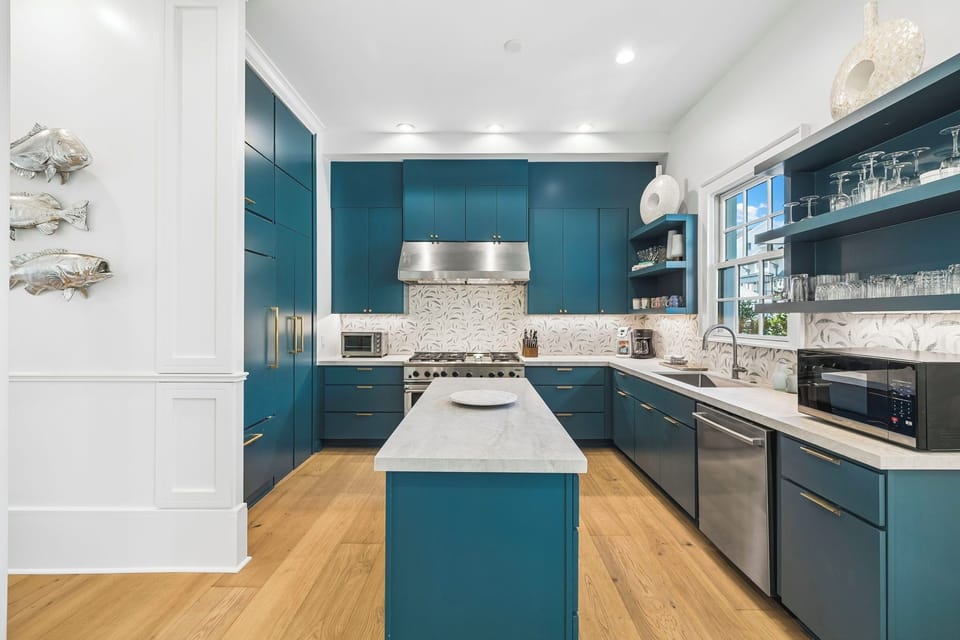 Your chef-worthy kitchen features rich teal cabinetry, a spacious central island with marble countertops, and professional-grade stainless appliances ready to inspire your culinary adventures.