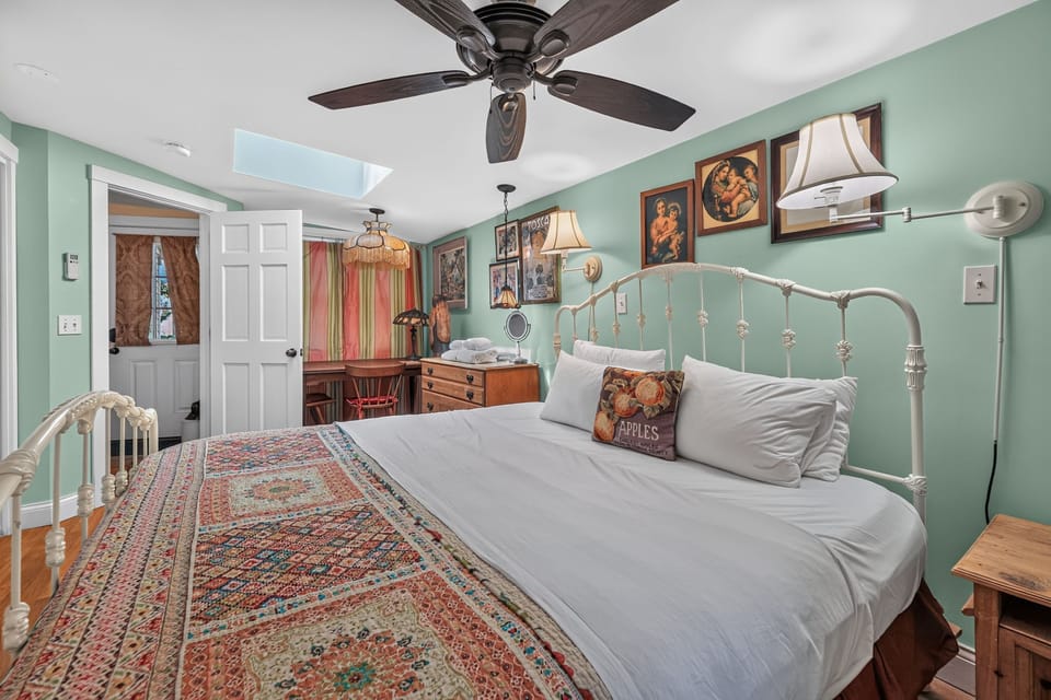 A cozy bedroom with pale green walls, a white metal bed, and eclectic decor.