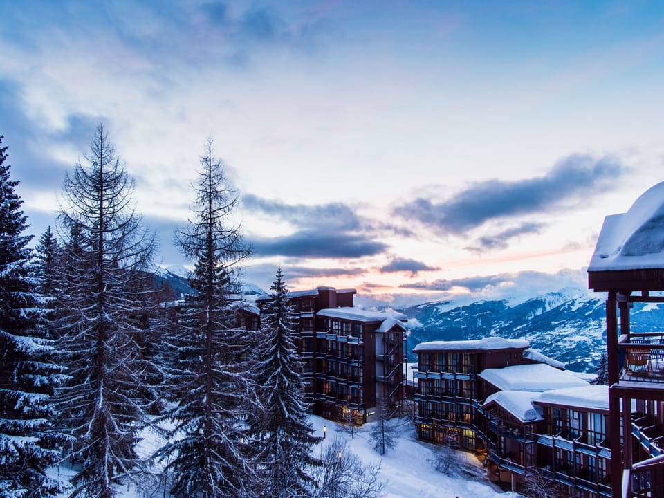 Snow-dusted pines and residence buildings glowing under a sunset sky