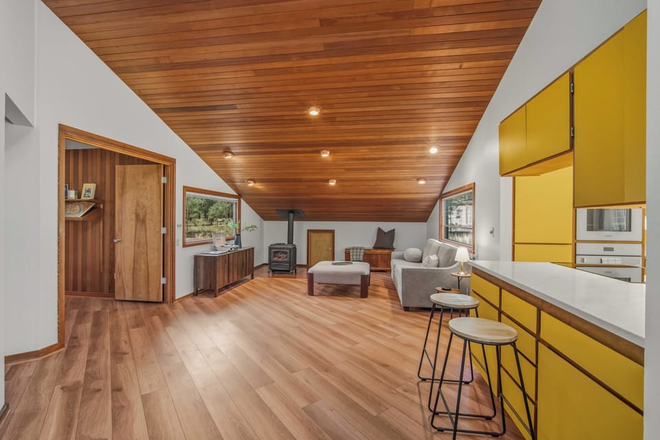 Warm wood ceilings and gleaming floors define this open-concept retreat, with a cozy fireplace anchoring the living space. Modern yellow cabinetry adds cheerful color to the sleek kitchen—perfect for relaxed mornings in this stylish mountain escape.