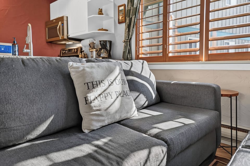 Sink into your happy place on this cozy sofa where natural light streams through wooden shutters. The warm, inviting living area flows seamlessly into the well-equipped kitchen, ready for your home-cooked meals.
