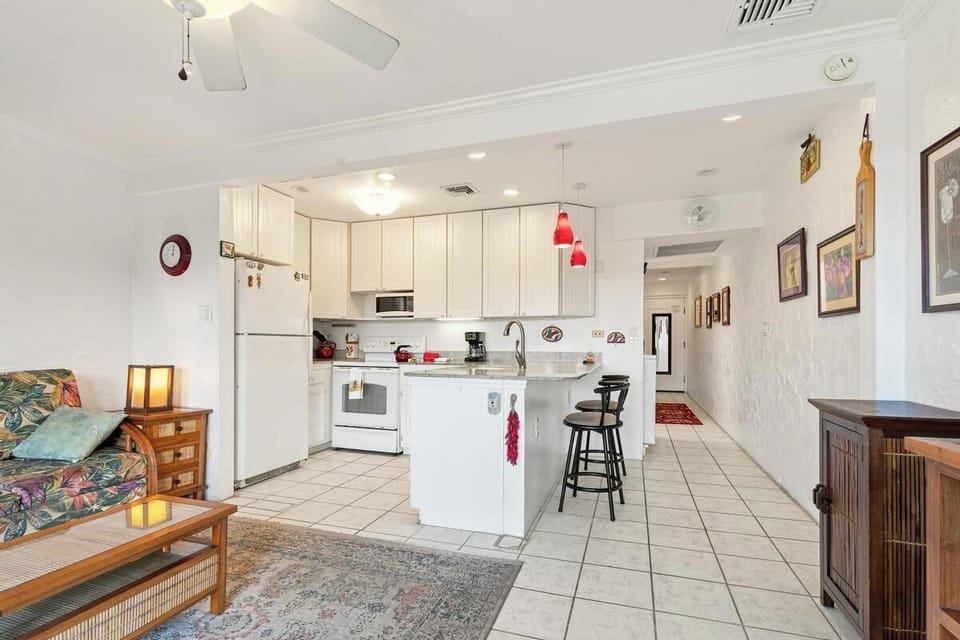 Step into your bright, open living space where the kitchen flows seamlessly into your cozy sitting area—perfect for preparing tropical drinks while you unwind.