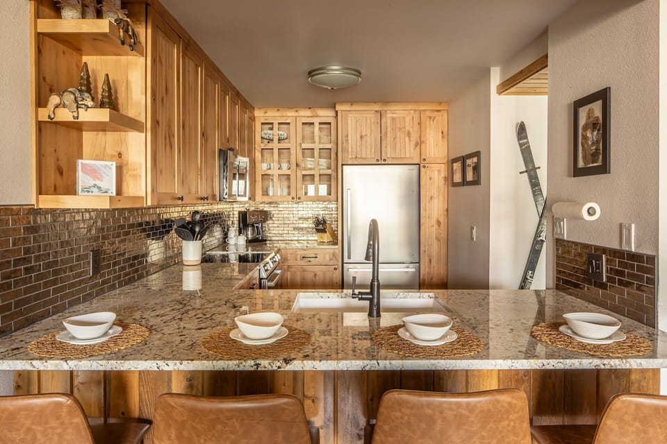 Gather around the spacious granite breakfast bar where four leather-upholstered stools invite morning coffee or evening conversation. Warm wood cabinets and gleaming tile backsplash create a welcoming alpine atmosphere in your fully-equipped kitchen.