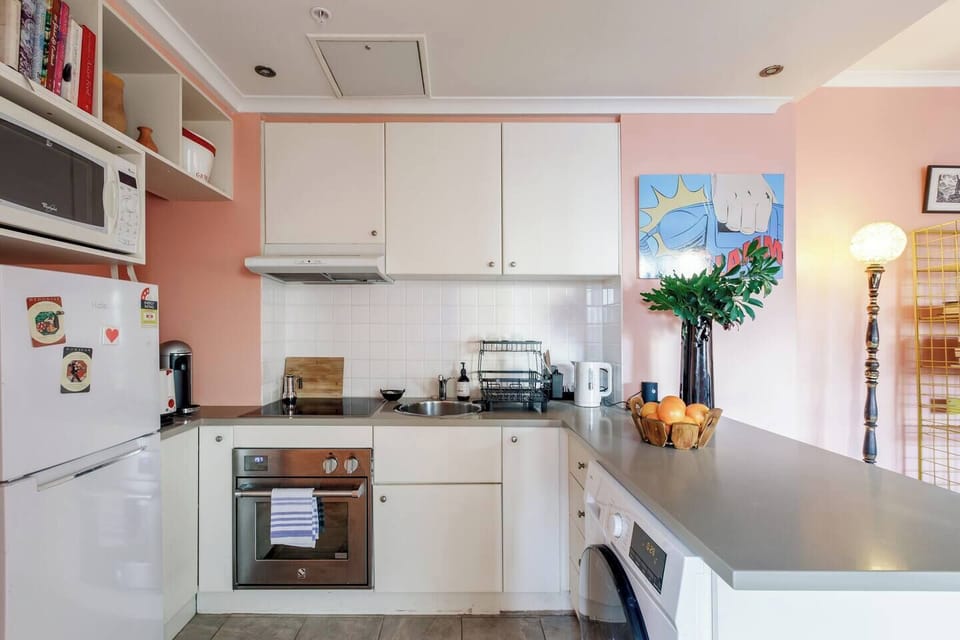 Prepare meals in the well-equipped kitchen, complete with an oven, coffee machine, open shelving, and all the essentials for everyday cooking. A washer is neatly tucked below for added convenience.