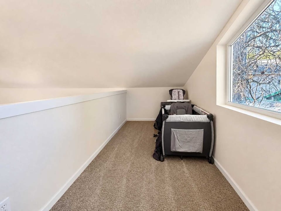 Upper-level loft with a low, sloped ceiling, large window, pack and play, and high chair for families traveling with young children.