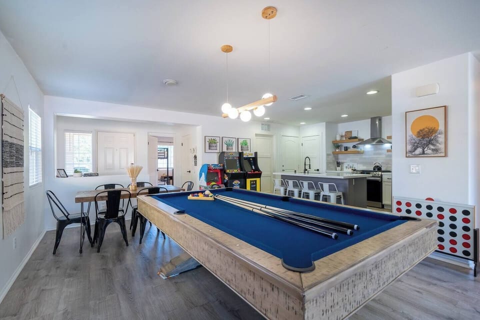 Open-concept dining/living/kitchen area with seating for 6 at the dining table plus 4 at the kitchen island, along with a pool table, arcade games, and giant Connect Four—perfect for families and groups in Indio.
