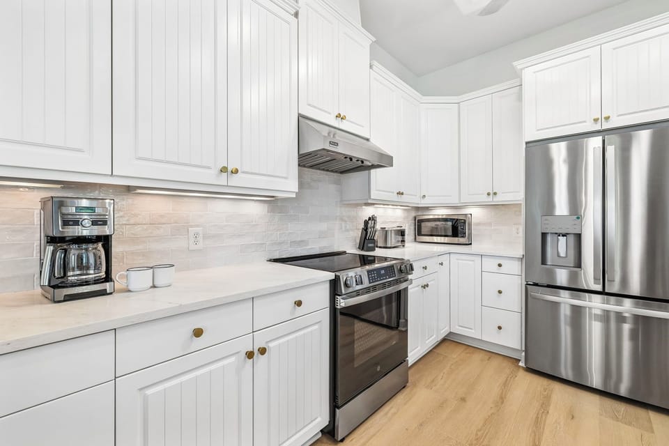 Step into your bright, fully equipped kitchen with gleaming stainless steel appliances, crisp white cabinetry, and warm wood floors—ready for your morning coffee or home-cooked meals during your stay.