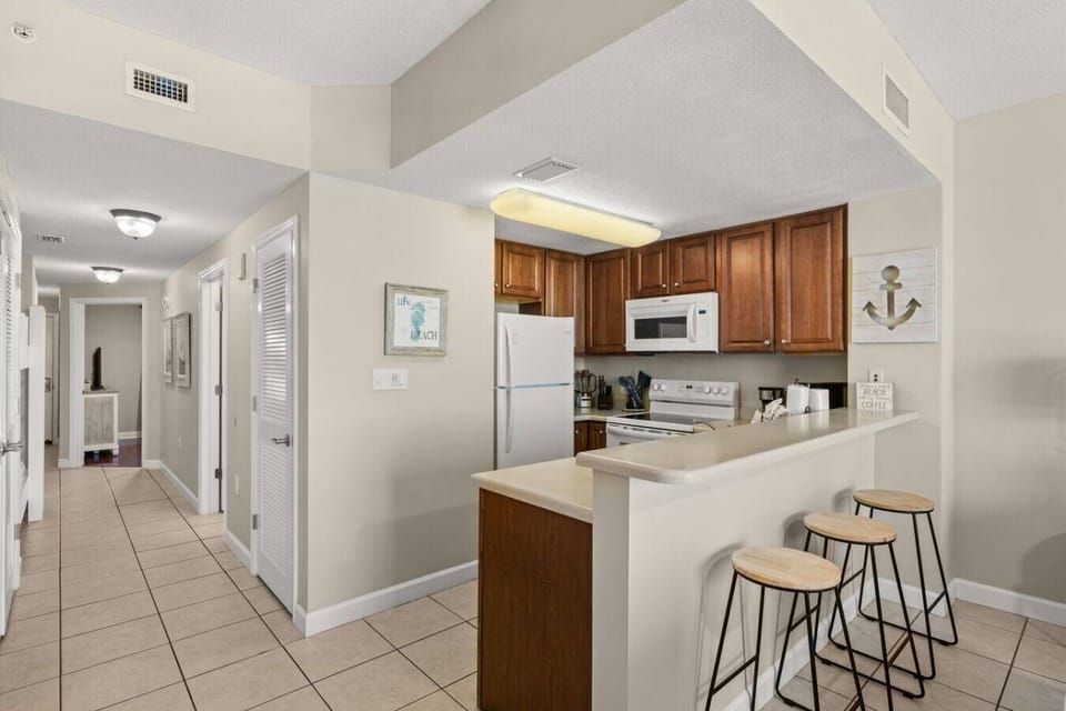 Pull up a stool at the breakfast bar beside the full kitchen, with warm wood cabinetry and convenient access from the hallway.