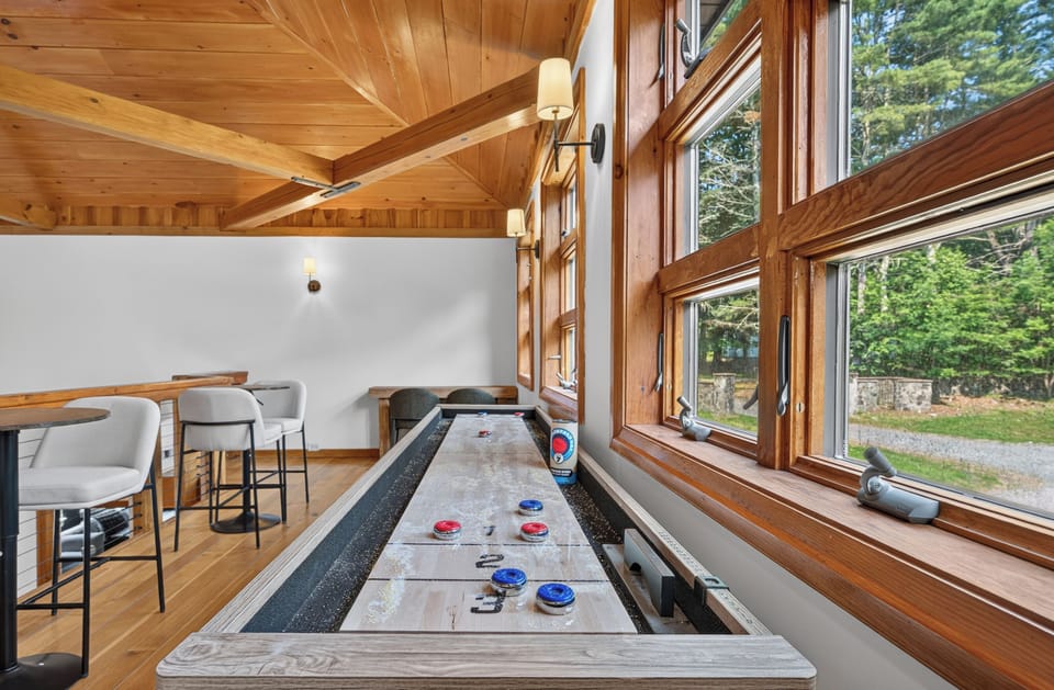 Bright loft game area with shuffleboard, bar seating, and wooded views