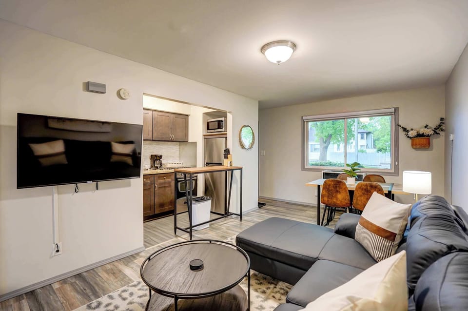 Charming and comfortable living space featuring a plush sectional, wall-mounted 55" Roku Smart TV, and dining area with large windows for a welcoming, relaxed atmosphere.
