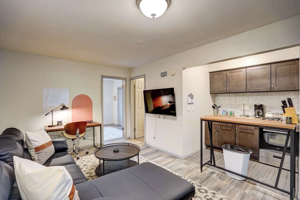 Inviting open-concept space featuring a modern kitchen, cozy sectional, mounted 55" Roku Smart TV, and dedicated workspace—perfect for relaxing, cooking, or getting a little work done during your stay.