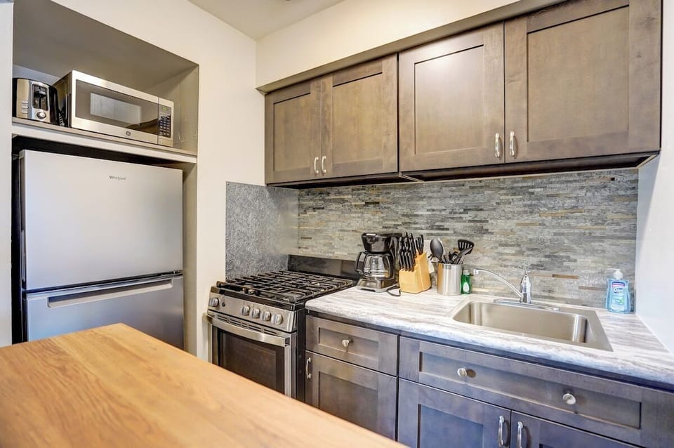 Sleek, fully equipped kitchen featuring stainless steel appliances, gas range, modern stone backsplash, and all the essentials for cooking at home—perfect for quick meals or longer stays.