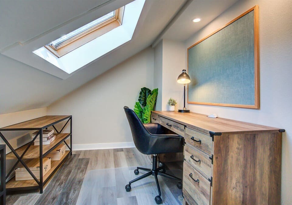 Bright, tucked-away workspace featuring a skylight for natural light, a sturdy wood desk with ample drawers, and a modern chair—perfect for focused work or study sessions.