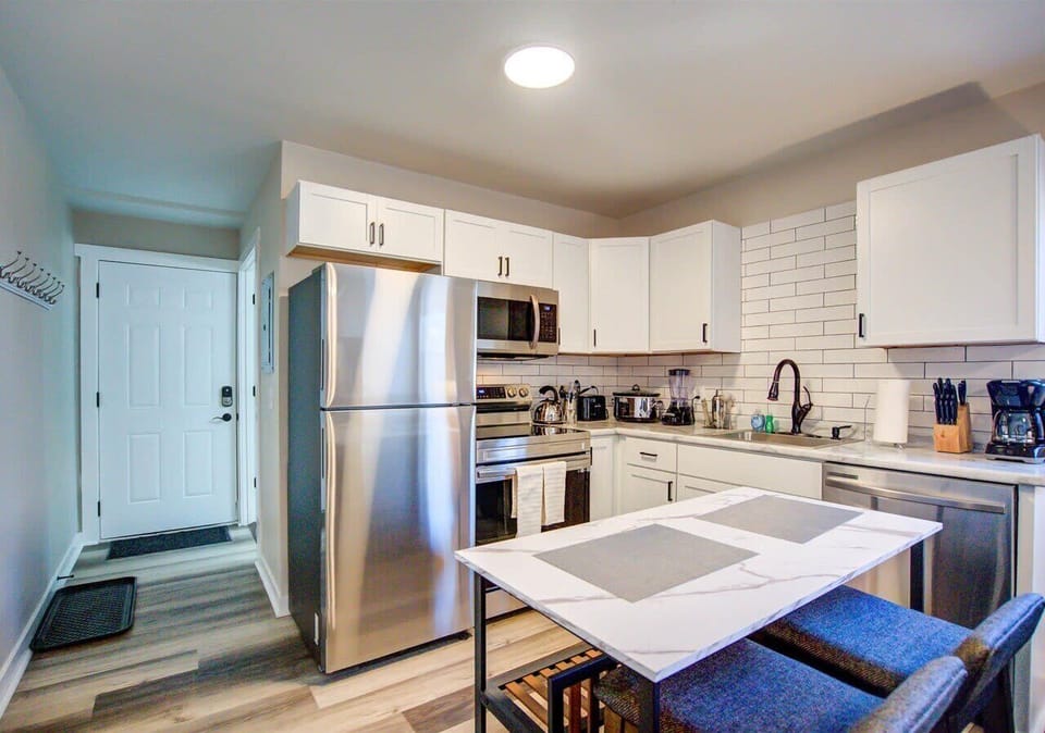 Modern kitchen with sleek stainless steel appliances, white subway tile backsplash, and a dining table for four. Perfect for a medium-term stay, offering all the essentials for cooking and entertaining in a bright, open space