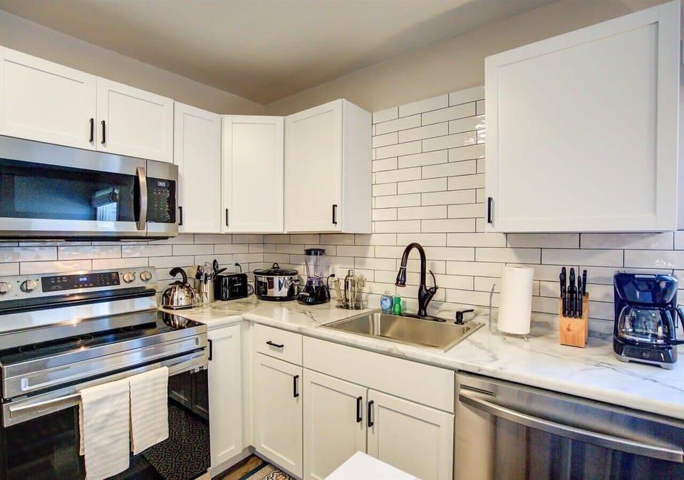 Bright, fully equipped kitchen with stainless steel appliances, subway tile backsplash, and ample counter space. Includes cookware, coffee maker, and essentials for preparing meals with ease.