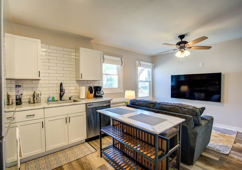 Open-concept layout with kitchen and living room seamlessly connected. Features a central island for dining or prep, cozy seating, and a large wall-mounted TV—perfect for relaxing or entertaining.