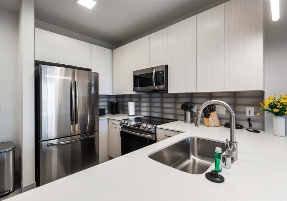 Contemporary kitchen with stainless steel appliances, a sleek tile backsplash, and crisp white cabinetry. The spacious island and modern fixtures create a stylish and functional space for cooking or entertaining.