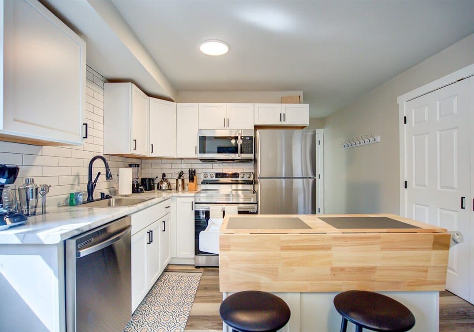 Bright, modern kitchen with sleek stainless steel appliances, white shaker cabinets, and a stylish subway tile backsplash. Features a wooden island with seating for two, perfect for casual meals or extra prep space.